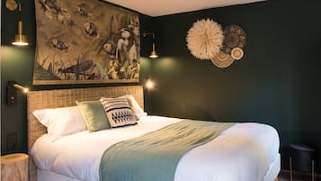 Ein großes Bett mit weißen Leinen und einer grünen Tagesdecke, das von zwei Nachttischen mit Lampen eingerahmt wird. Ein Wandbild zeigt Fische und ein dekoratives Wandelement.
