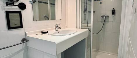 A modern bathroom with a white sink, mirror, and glass-enclosed shower.