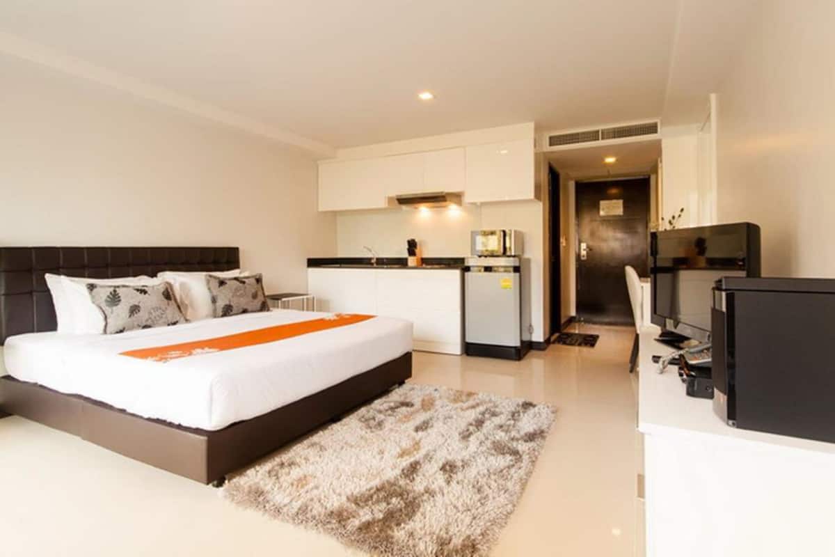 A modern hotel room with a large bed, a small kitchenette, and a separate desk area.