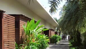 A corridor with a concrete floor, wooden slatted walls, and lush green plants. - The Kris Resort Condotel at Bagtao Beach (Choeng Thale)