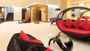 A spacious room with a large seating area featuring a wicker chair and a sofa with red cushions. A pool table is visible in the background. - The Kris Resort Condotel at Bagtao Beach (Choeng Thale)