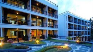 A modern hotel with multiple floors, a landscaped garden, and a well-lit entrance. - The Kris Resort Condotel at Bagtao Beach (Choeng Thale)