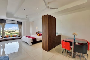 Habitación de hotel con cama, escritorio con sillas, ventilador de techo y vista al exterior.