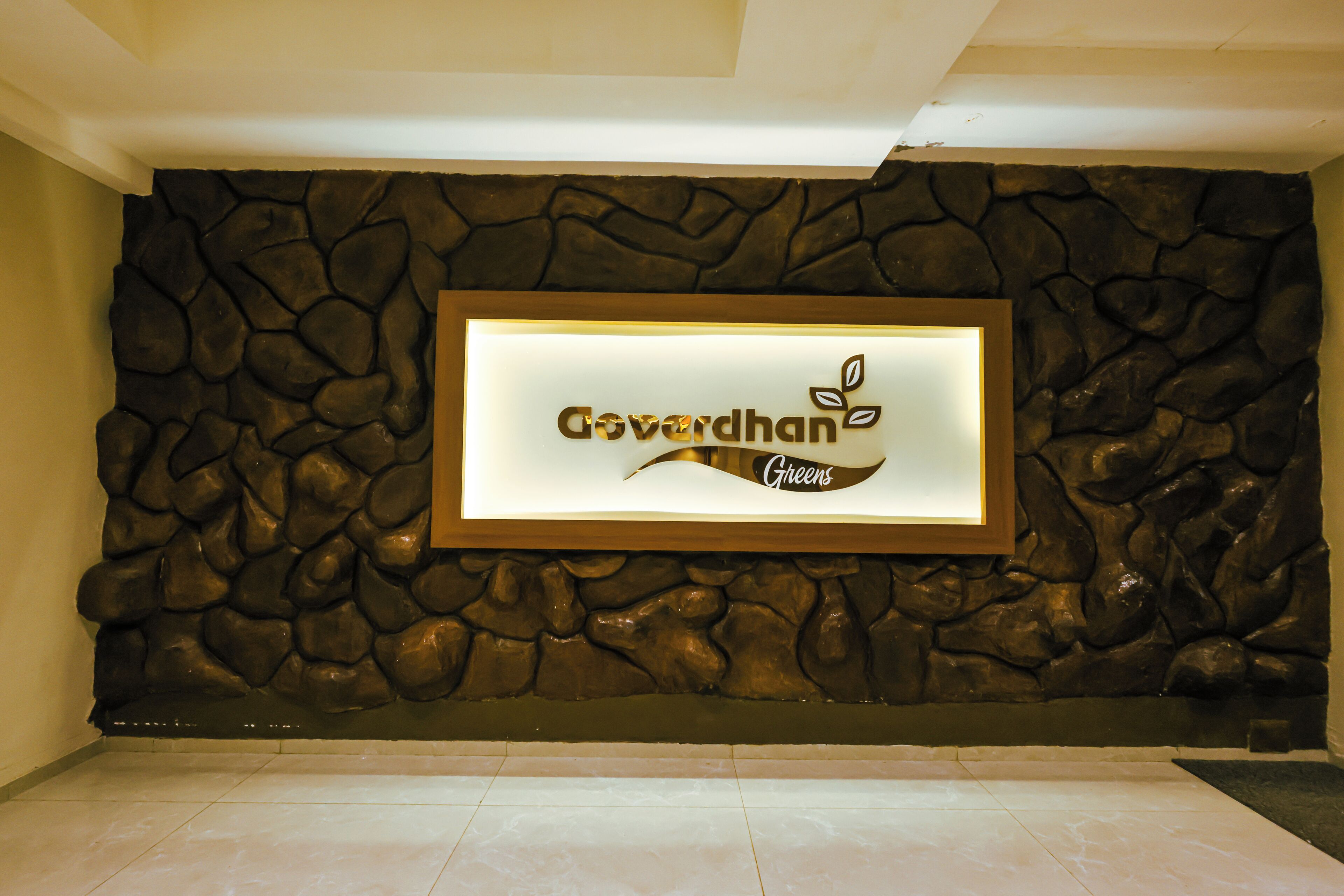 Un cartel en marco con el texto 'Govardhan Greens' frente a una pared con textura.