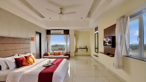 A hotel room with a bed, a TV, a window, and a ceiling fan. - Goverdhan Greens Resort Dwarka (Dwarka)