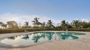 A swimming pool with a tiled deck, surrounded by palm trees and greenery. - Goverdhan Greens Resort Dwarka (Dwarka)