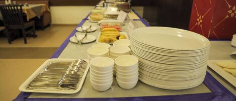 A buffet setup with plates, bowls, and utensils.
