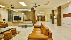 A spacious living area with a large sofa, a television, and a staircase leading to an upper floor. - Goverdhan Greens Resort Dwarka (Dwarka)