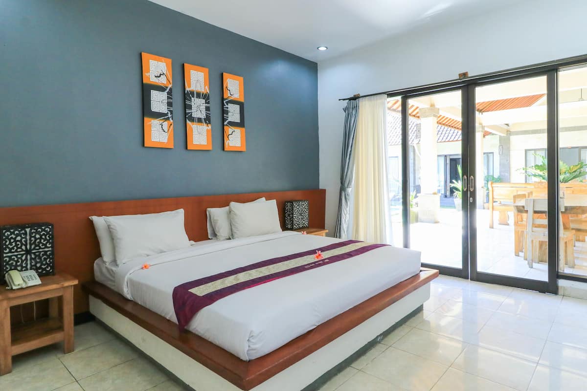 A hotel room with a large bed, a wooden nightstand with a phone, and artwork on the wall.