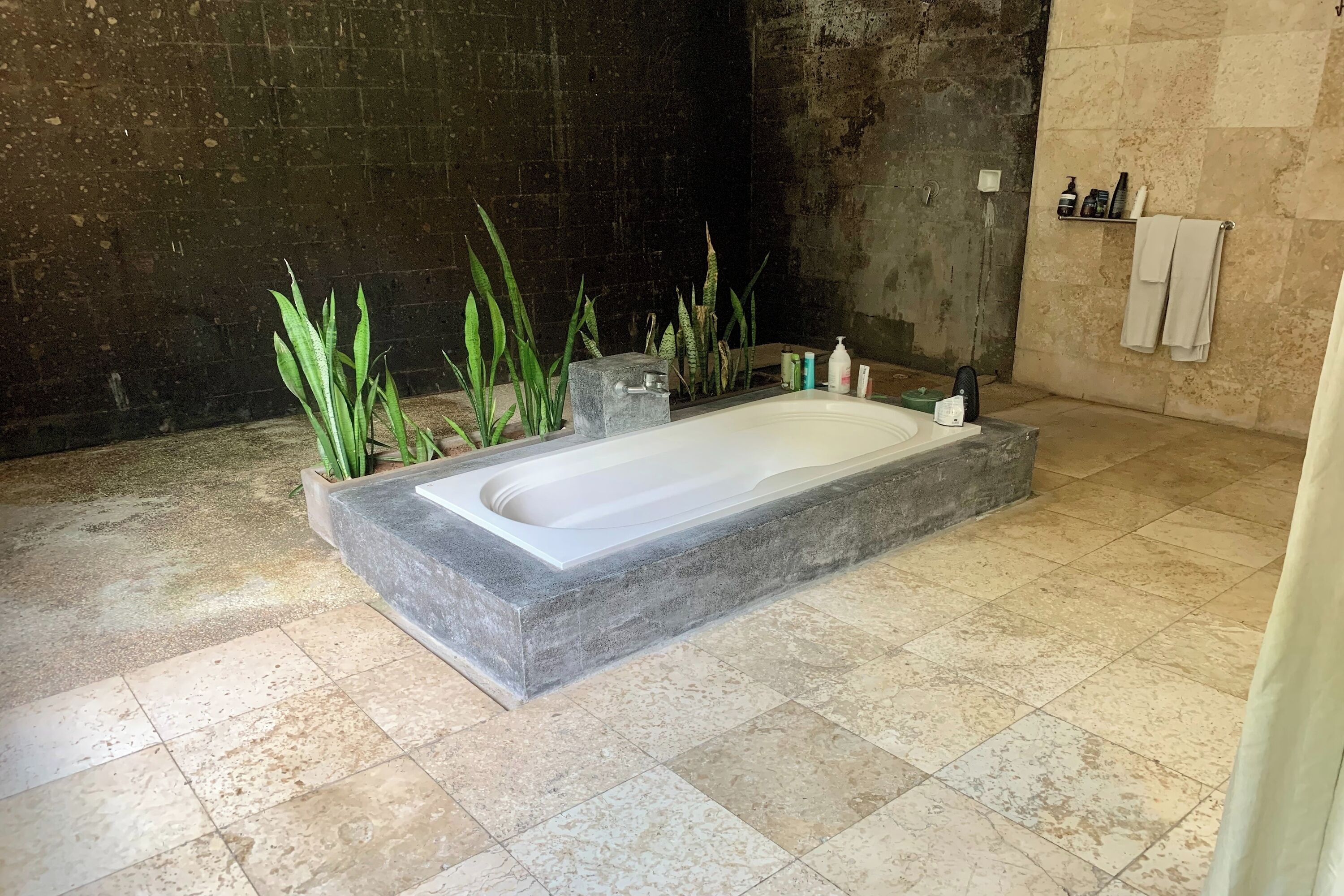 Un baño moderno con una bañera rectangular, plantas verdes y un estante con artículos de aseo.