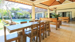 Un patio exterior con mesas y sillas de madera, una piscina y vistas de los edificios circundantes.