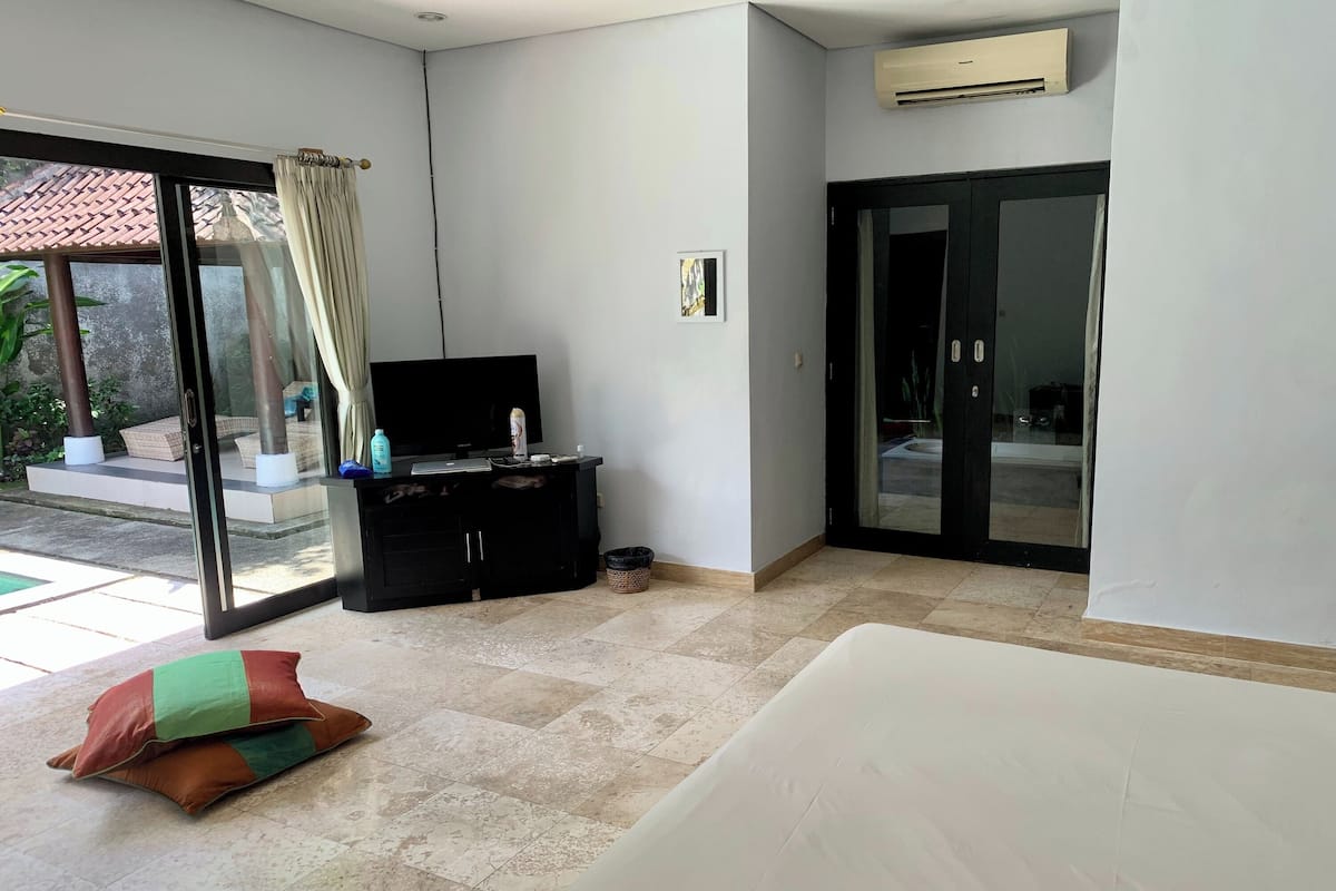 A modern hotel room with a large sliding glass door leading to a patio, a black entertainment unit, and a white sofa.