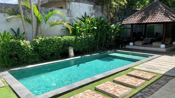 Una piscina rectangular con agua azul cristalina, rodeada por un borde de piedra y una zona verde con piedras para pisar.