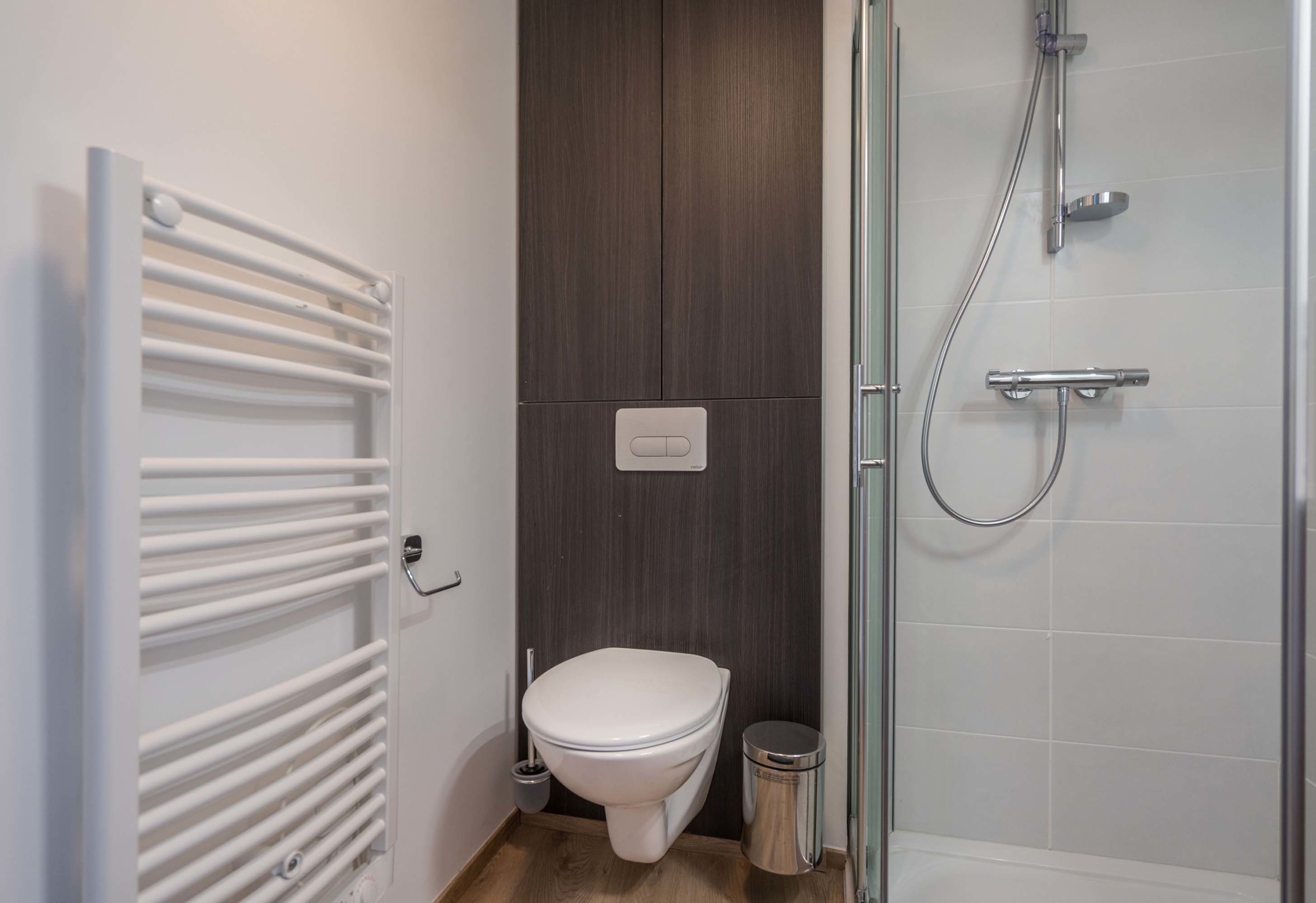 A bathroom with a white toilet, a shower, and a towel rack.