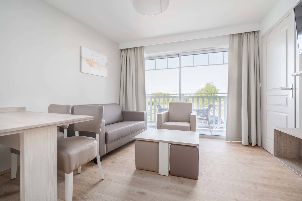 Una sala de estar moderna con comedor, un sofá, una mesa de centro y un balcón con cortinas.