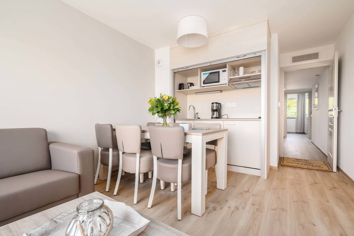 Un espacio habitable moderno y compacto con kitchenette, un comedor con mesa y sillas, y un sofá.