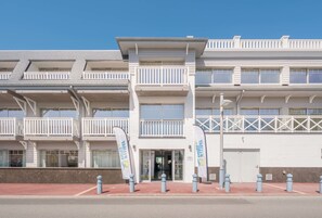 A multi-story hotel with balconies, a red-paved entrance, and white exterior walls.