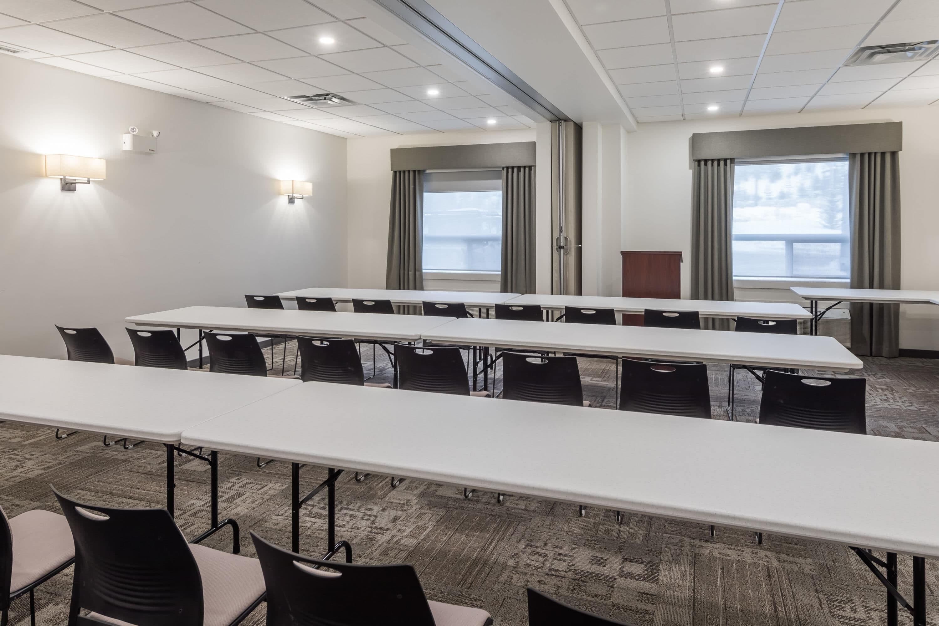 A conference room with long tables and chairs, large windows with curtains, and wall-mounted lighting.