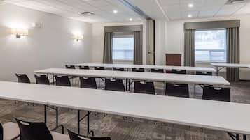 A conference room with long tables and chairs, large windows with curtains, and wall-mounted lighting.