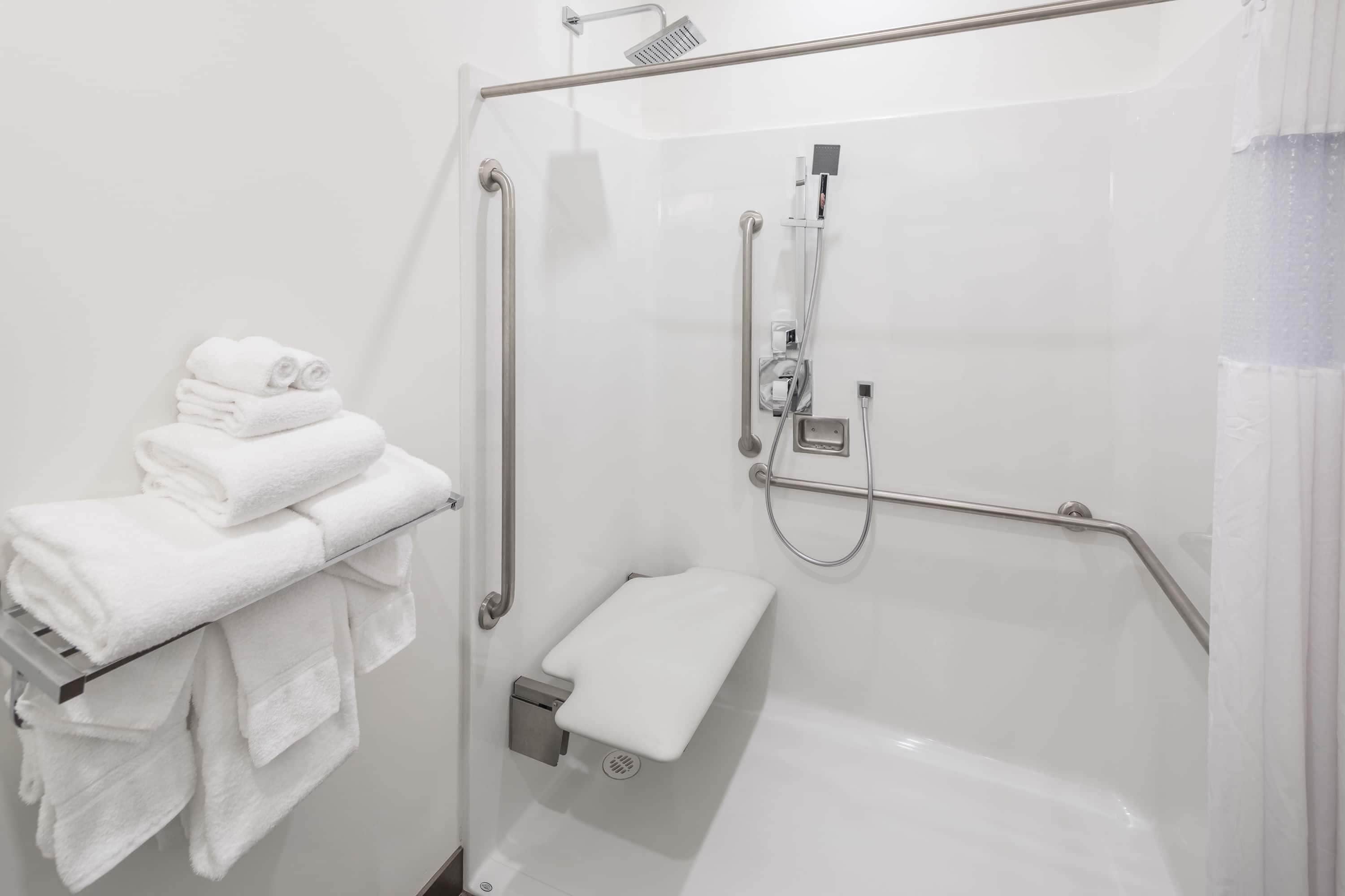 Een moderne badkamer met een douchecabine van glas, een handdoekrek met opgevouwen handdoeken, en een handdouche.
