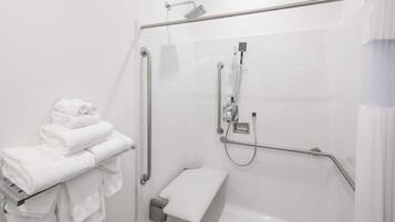 Un baño moderno con cabina de ducha de vidrio, un perchero con toallas dobladas y un cabezal de ducha manual.