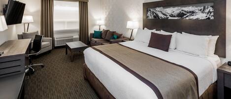 A hotel room with a large bed, a desk, a chair, a sofa, and a TV.