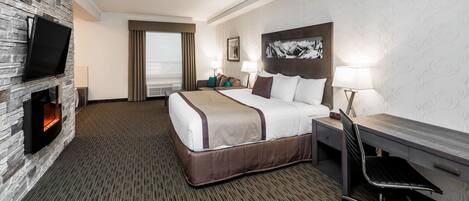 A hotel room with a bed, desk, chair, TV, fireplace, and a large window.