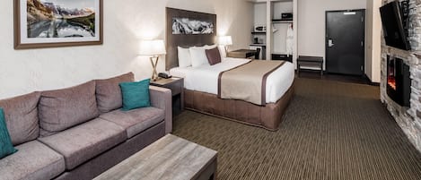 Une chambre d’hôtel avec un lit, un canapé, une table basse, une télévision, une cheminée et un tableau encadré au mur.