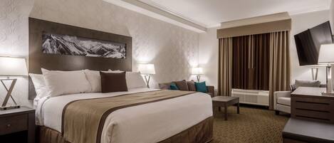 A hotel room with a large bed, two bedside tables with lamps, a flat-screen TV, a sofa, and a desk.
