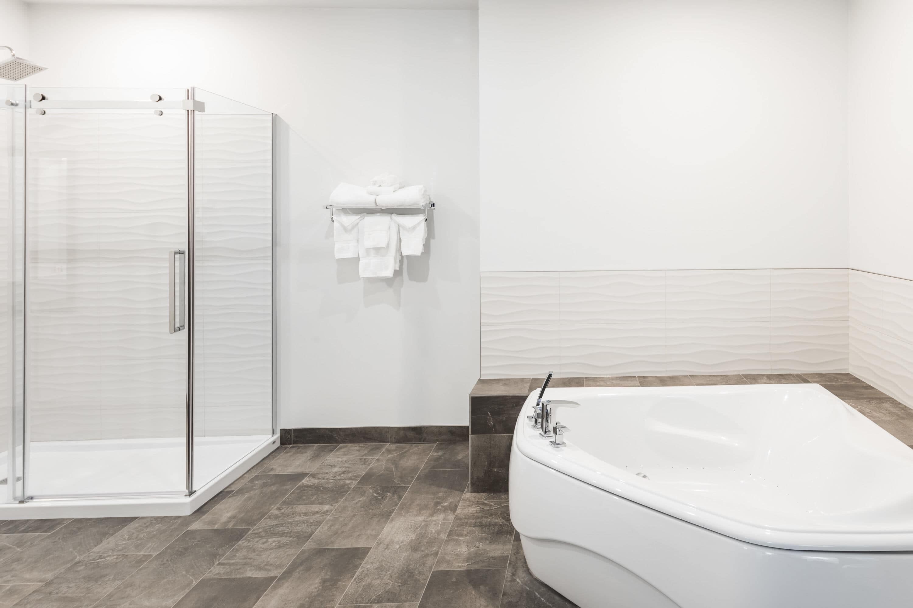 A modern bathroom with a glass shower enclosure, a white bathtub, and a towel rack with folded towels.