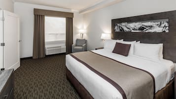 A hotel room with a large bed, a chair, a desk, and a window with curtains.