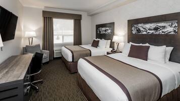 A hotel room with two beds, a desk, a chair, a TV, and artwork on the walls.