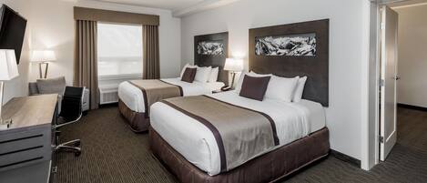 A hotel room with two beds, a desk, a chair, a TV, and artwork on the walls.