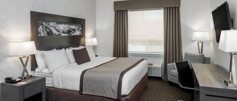 A hotel room with a bed, bedside tables, a desk, a chair, a TV, and a large window with curtains.