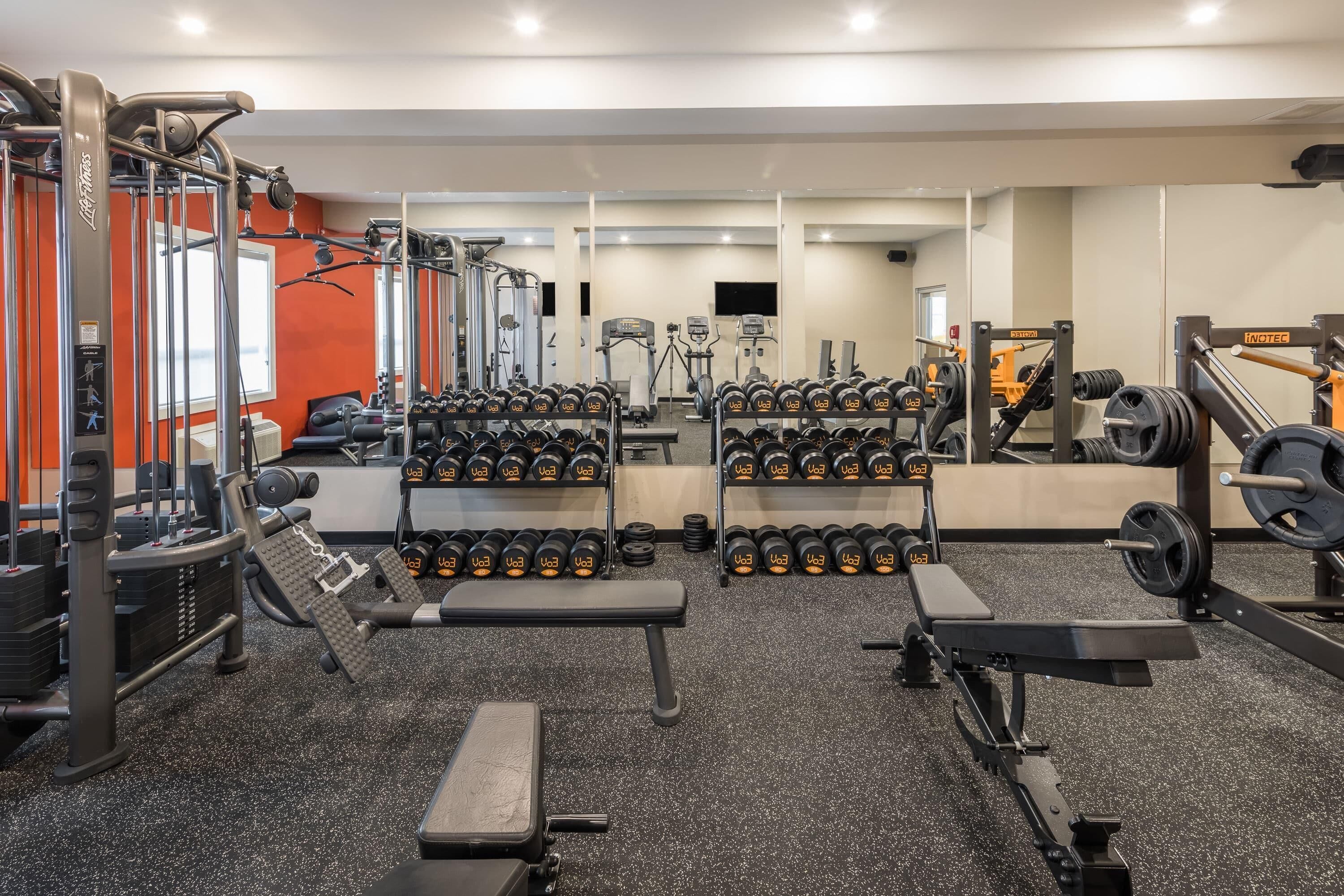 Un gimnasio con equipo de levantamiento de pesas, cintas de correr y mancuernas.
