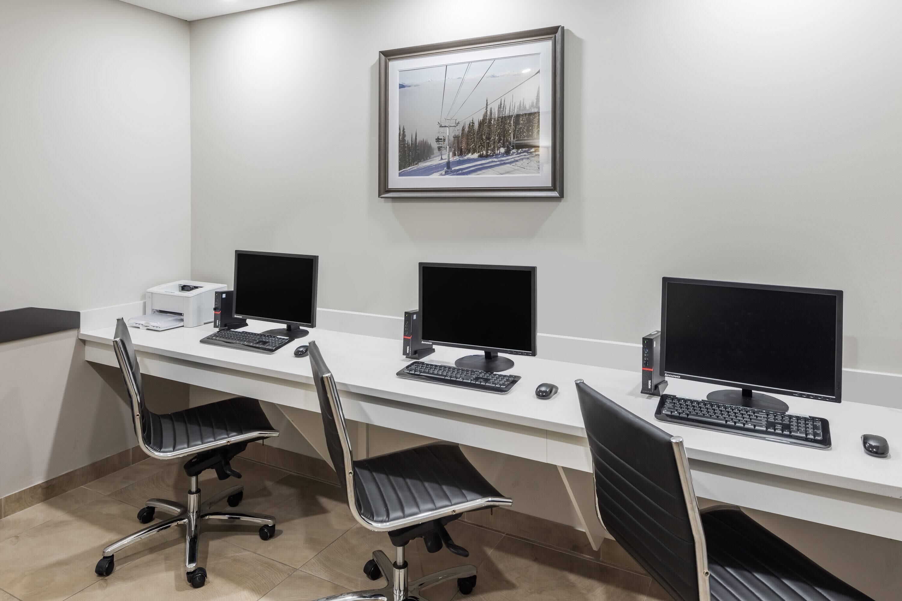 Una sala de conferencias con tres escritorios, cada uno con una computadora, teclado y ratón. Hay dos sillas de oficina y un cuadro en la pared.