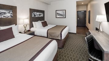 A hotel room with two beds, a desk, a chair, a TV, and framed pictures on the walls.