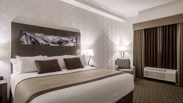 A hotel room with a large bed, two bedside tables, a chair, a wall-mounted TV, and a window with curtains.