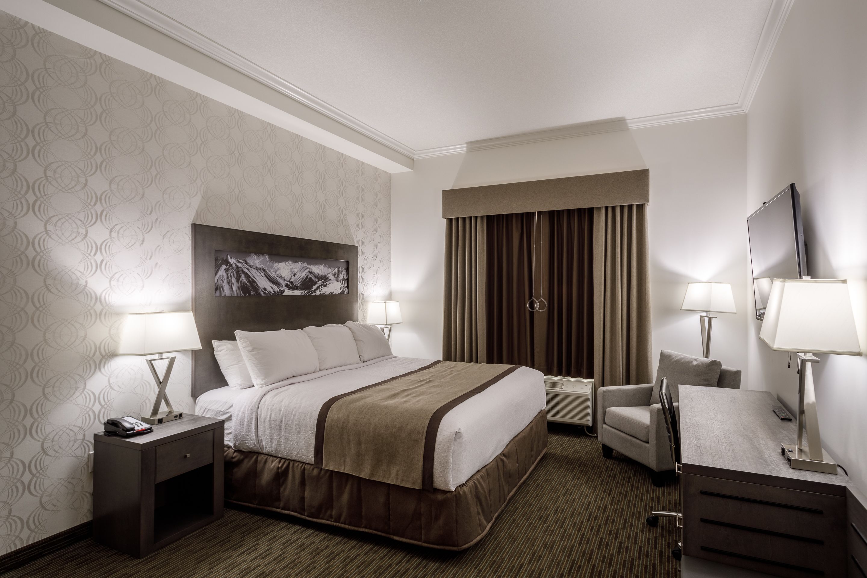 A hotel room with a large bed, two bedside tables with lamps, a desk with a chair, and a TV.