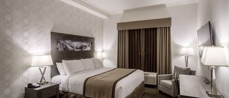 A hotel room with a large bed, two bedside tables with lamps, a desk with a chair, and a TV.