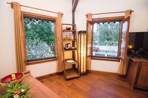 Una habitación con muebles de madera, una estantería con adornos, un farol y vista a una calle con árboles.