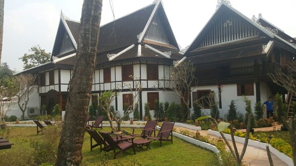 A traditional building with a symmetrical facade, multiple windows, and a well-maintained garden with chairs and trees. - Royal Peacock Boutique Hotel (Luang Prabang)