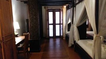 Una habitación con piso de madera, un escritorio con lámpara, una cama con dosel y una puerta que da a otra habitación.
