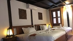 Una habitación de hotel con una cama grande, dos mesitas de noche, un aire acondicionado y una ventana con cortinas.