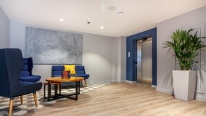 A modern lobby with a map mural, a seating area with blue chairs, a wooden table, and a potted plant. - Holiday Inn Express Wigan by IHG (Wigan)