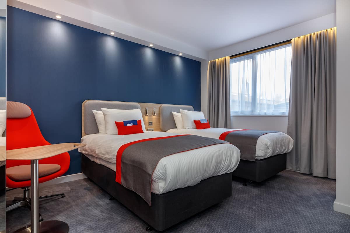 A hotel room with two beds, a red chair, and a large window with curtains.
