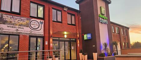 A Holiday Inn Express hotel with a visible entrance, signage for a Wheel Deal EV charging promotion, and a brick facade.