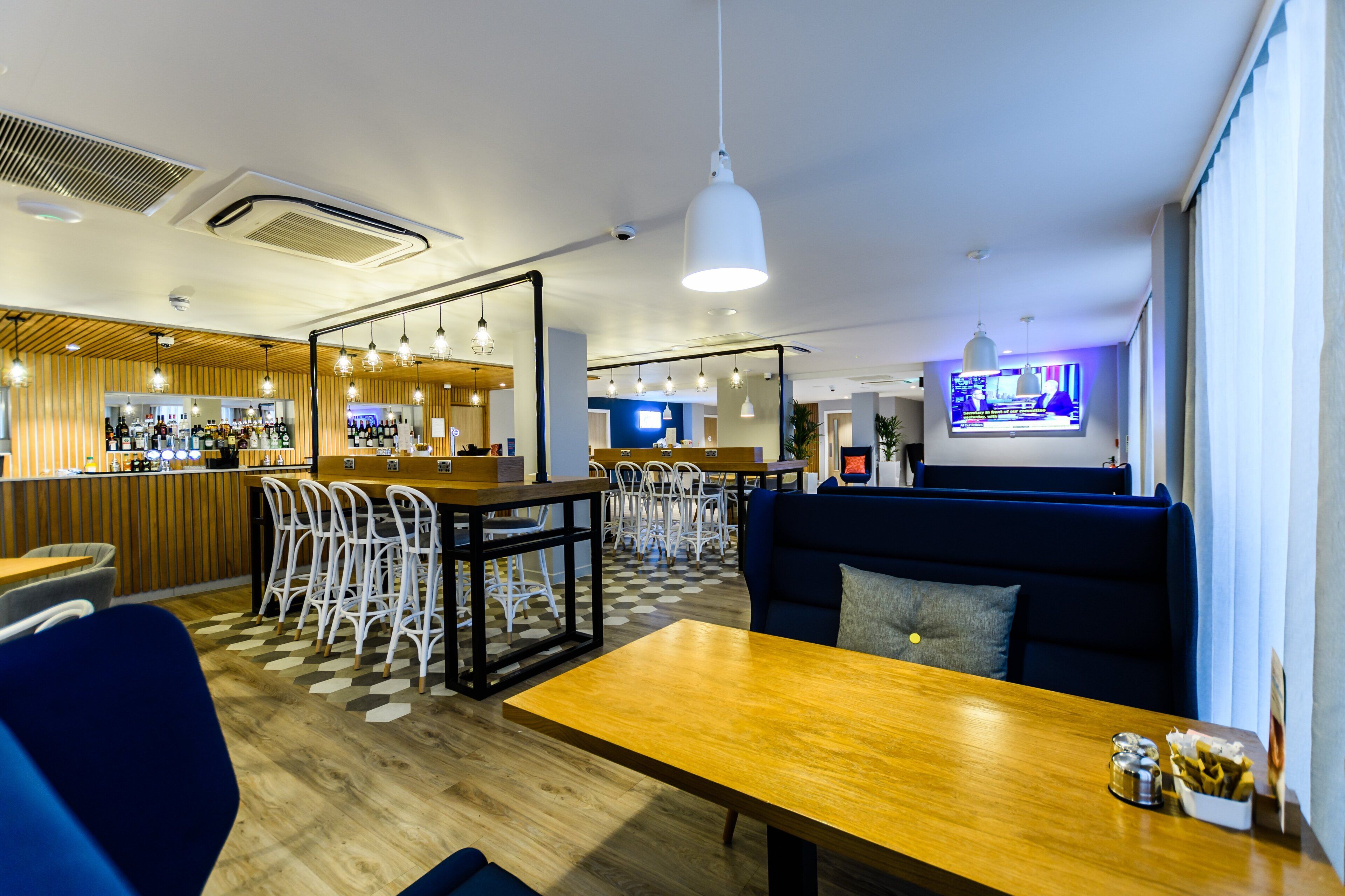 A modern bar area with wooden accents, seating arrangements, and a television screen.