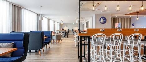 A modern hotel lobby with blue seating, a wooden reception desk, and a mix of white and grey chairs.
