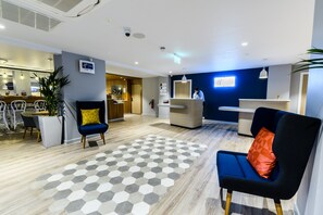 Un espace d’accueil d’hôtel au design moderne, comprenant un comptoir d’accueil, un coin salon et un bar.